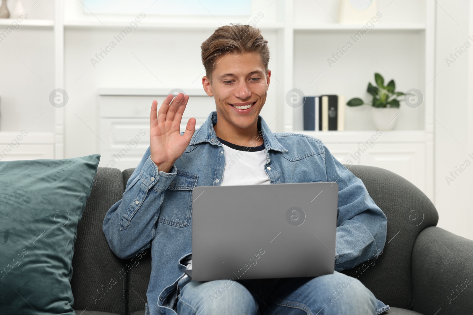 Photo of Happy young man having video chat via laptop on sofa indoors