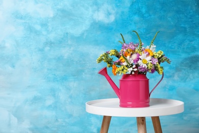 Photo of Watering can with beautiful wild flowers on table against color background