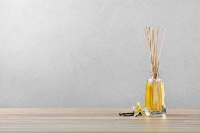 Photo of Reed air freshener with vanilla flower and sticks on wooden table against grey background. Space for text
