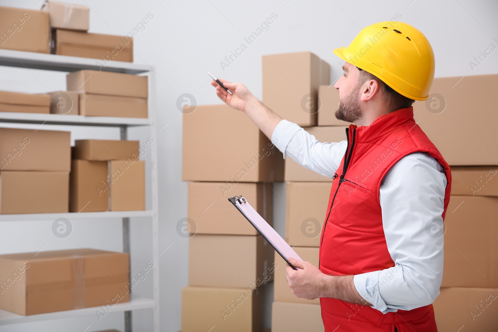 Photo of Young man with clipboard near cardboard boxes at warehouse