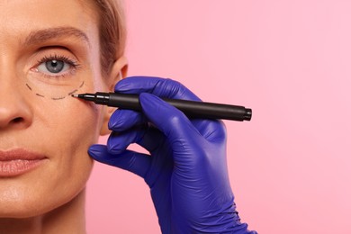 Doctor with marker preparing patient for cosmetic surgery operation on pink background, closeup. Space for text