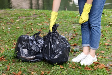 Woman holding plastic bags with garbage in park, closeup.