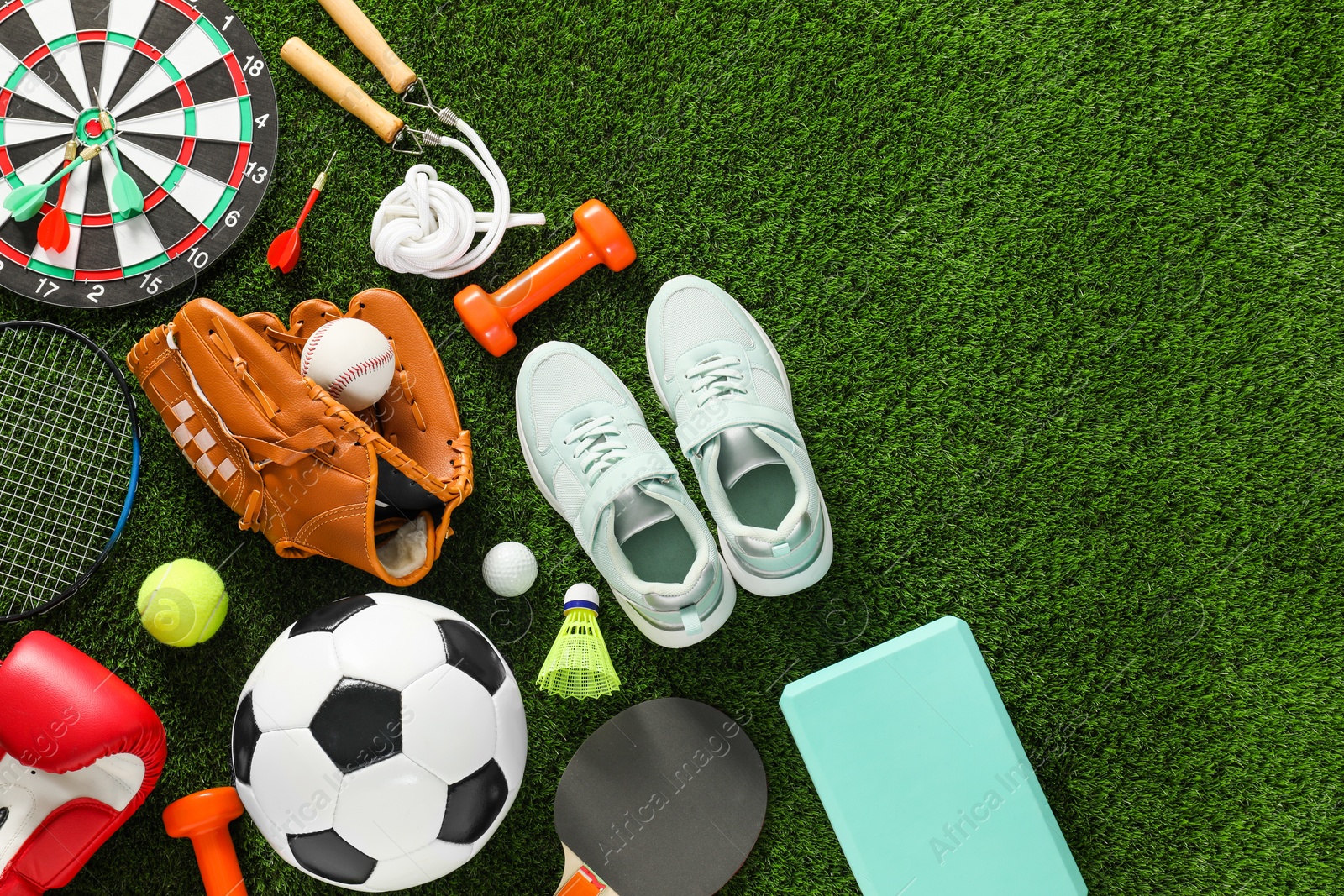 Photo of Different sport equipment and sneakers on green grass, flat lay. Space for text