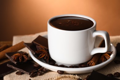 Photo of Cup of delicious hot chocolate, spices and coffee beans on table