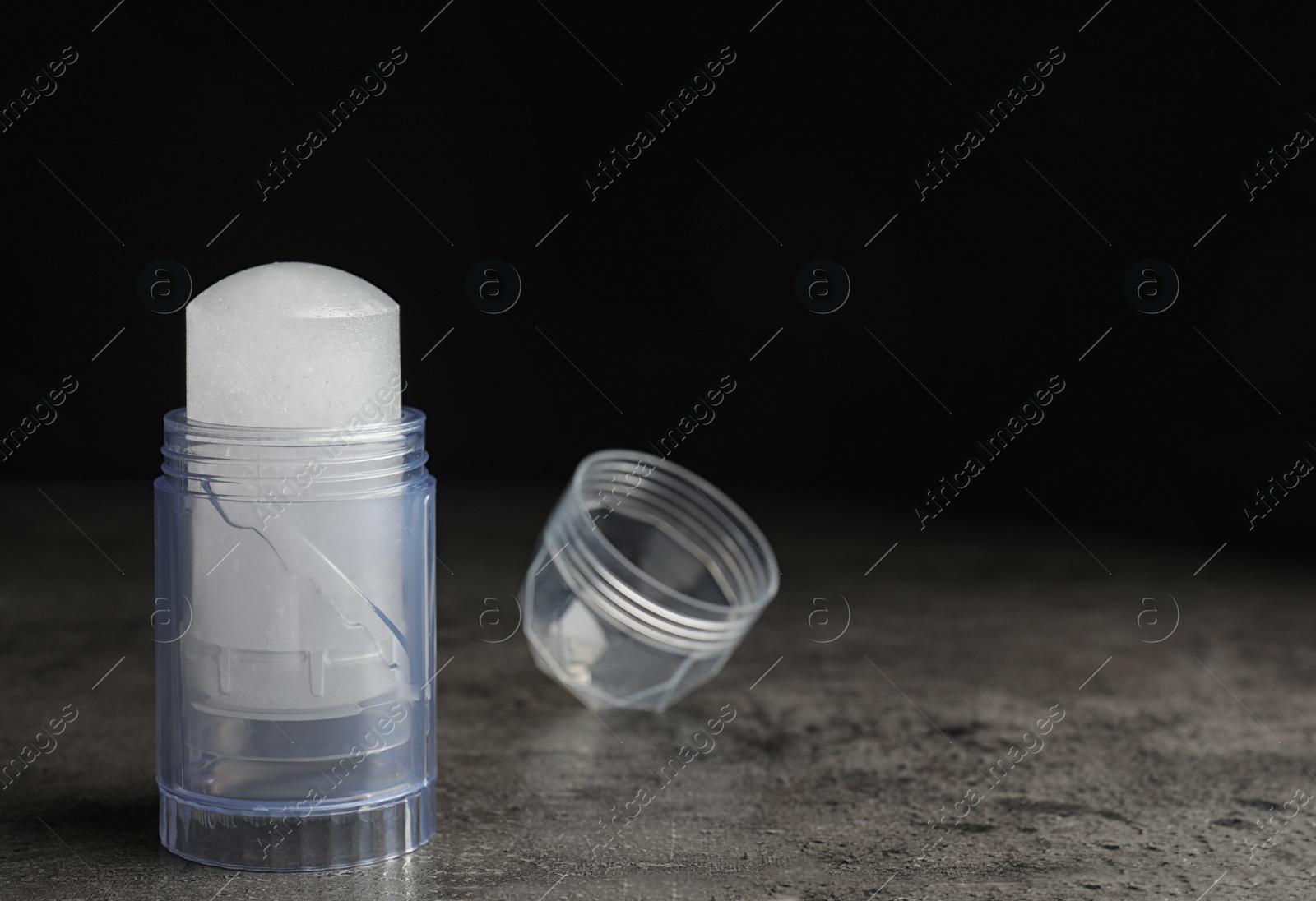 Photo of Natural crystal alum deodorant and cap on grey table, space for text