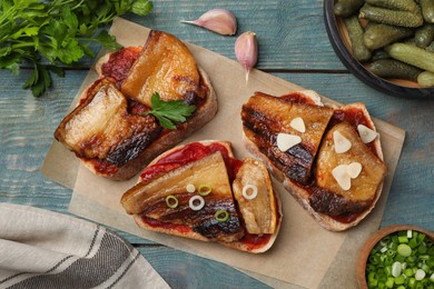 Photo of Tasty sandwiches with fried pork fatback slices on light blue wooden table, flat lay