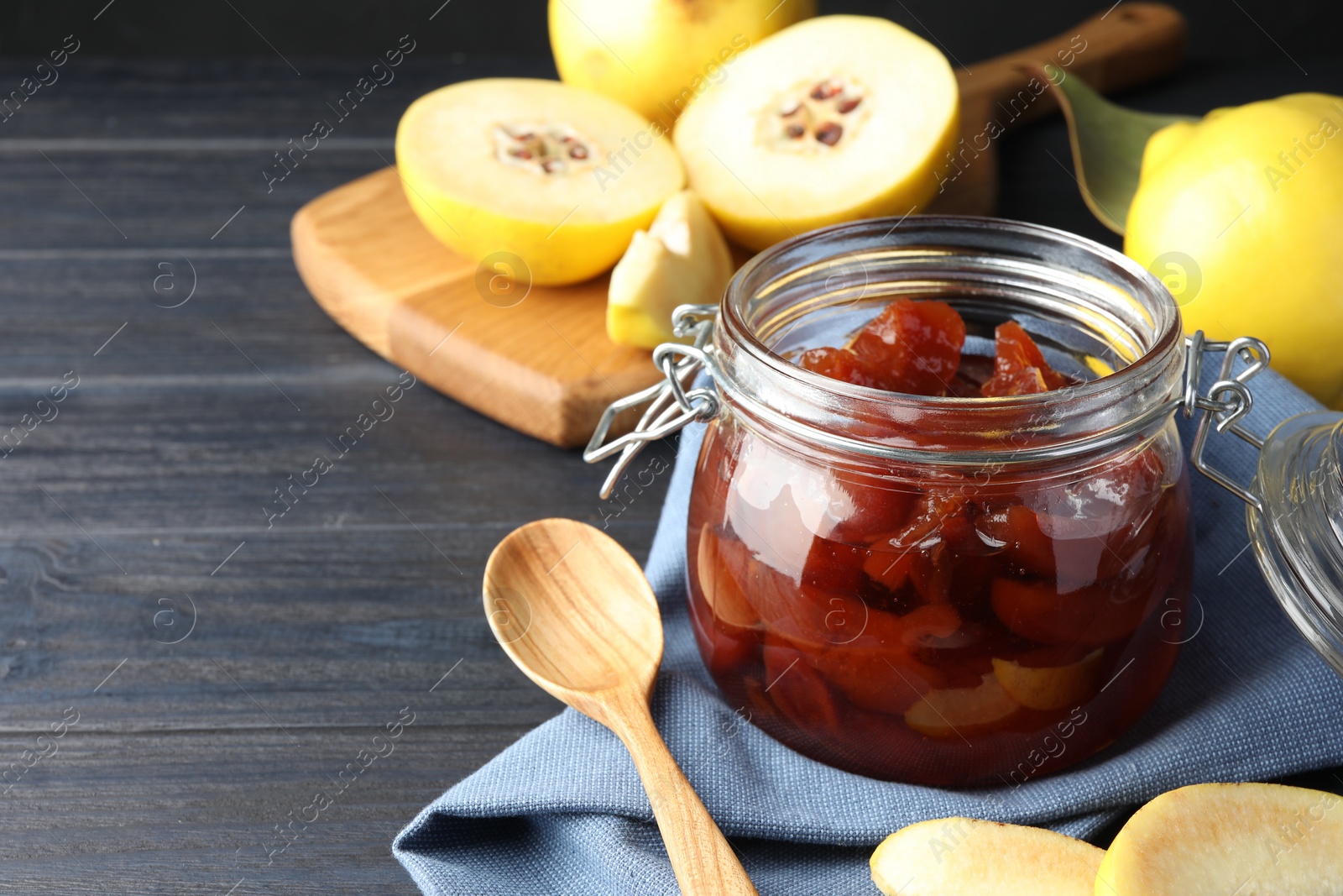 Photo of Quince jam in glass jar, spoon and fresh raw fruits on grey table, closeup. Space for text