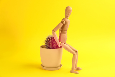 Hemorrhoid concept. Wooden human figure and cactus on yellow background