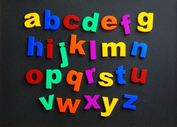 Photo of Colorful plastic magnetic letters on black background, top view. Alphabetical order