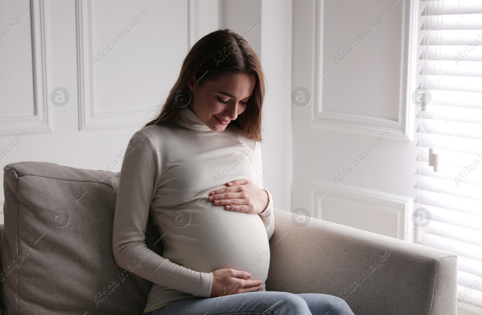 Photo of Young pregnant woman sitting on sofa at home