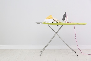 Photo of Board with modern iron and pile of clothes near light wall, space for text. Laundry day