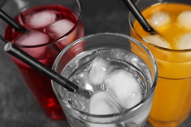Photo of Glasses of different refreshing soda water with ice cubes and straws on grey table, view from above