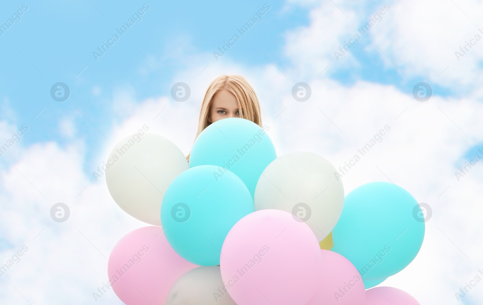 Photo of Beautiful young woman with bunch of balloons against blue sky