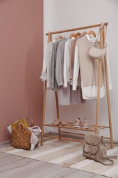 Photo of Rack with different stylish clothes and shoes near white wall in room