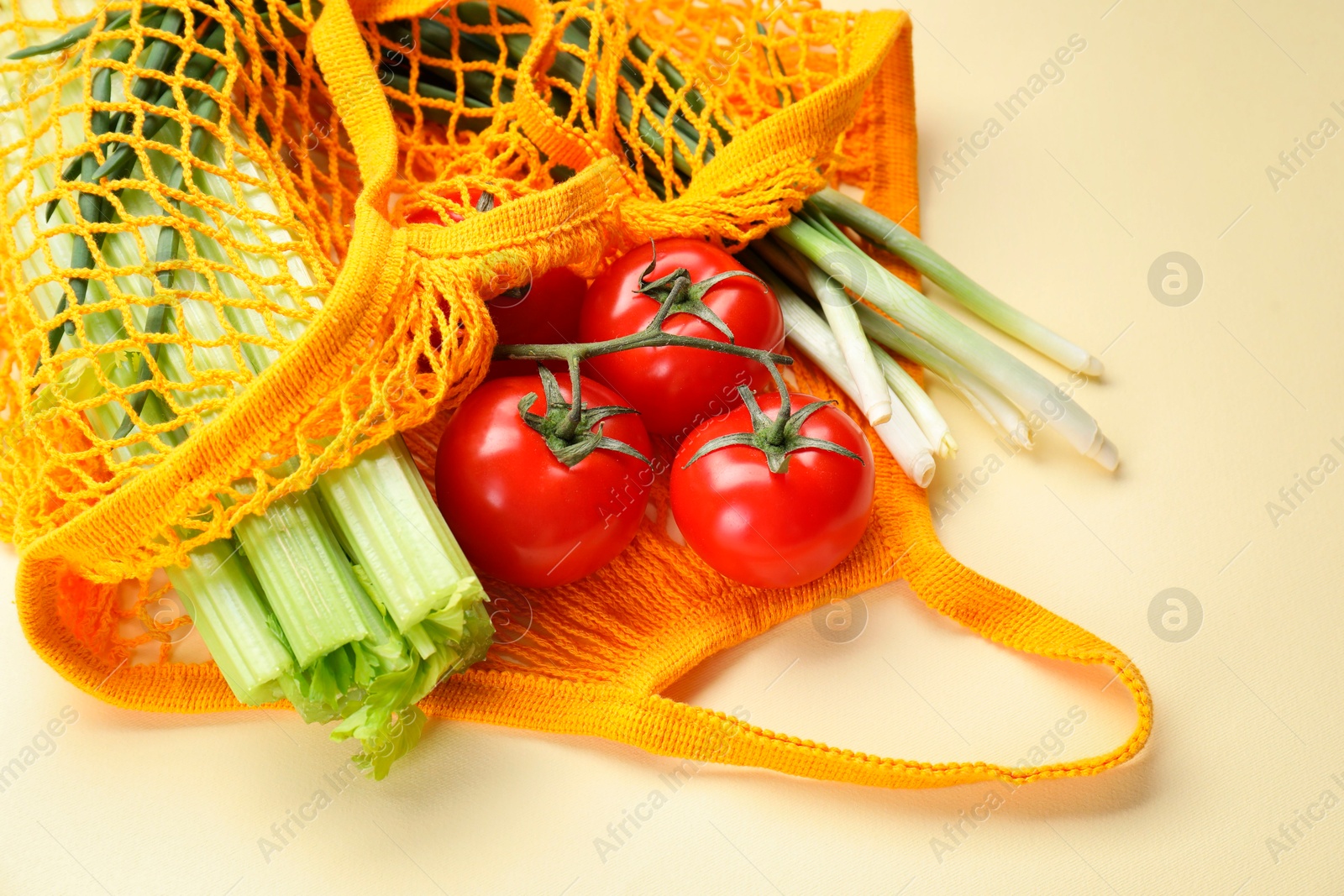 Photo of String bag with different vegetables on beige background, closeup