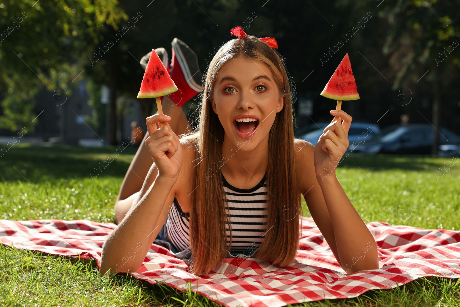 Photo of Beautiful girl with pieces of watermelon on picnic blanket in park