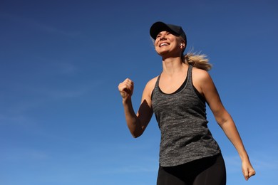 Woman listening to music while running outdoors in morning, low angle view. Space for text