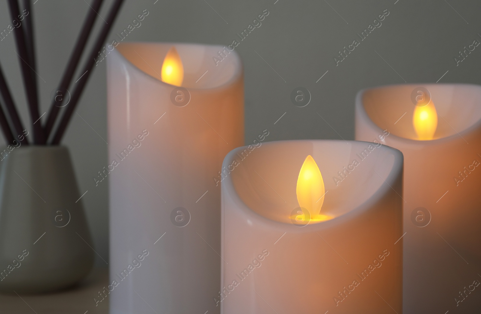 Photo of Glowing decorative LED candles on grey background, closeup view