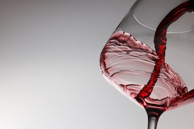 Photo of Pouring tasty red wine in glass on light background, closeup. Space for text