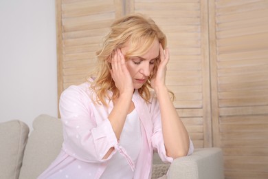 Photo of Woman suffering from headache on sofa at home. Hormonal disorders