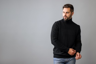 Photo of Handsome man in stylish black sweater on grey background, space for text