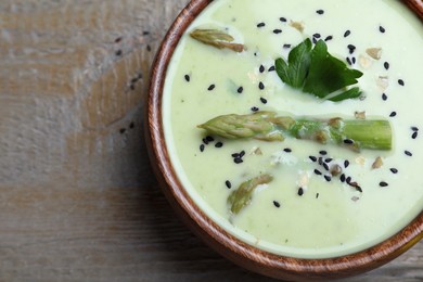 Photo of Bowl of delicious asparagus soup on wooden table, top view