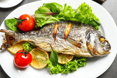 Photo of Delicious roasted fish with lemon and vegetables on plate, closeup view