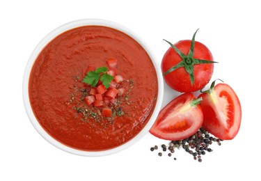 Delicious tomato cream soup with spices in bowl and tomatoes isolated on white, top view