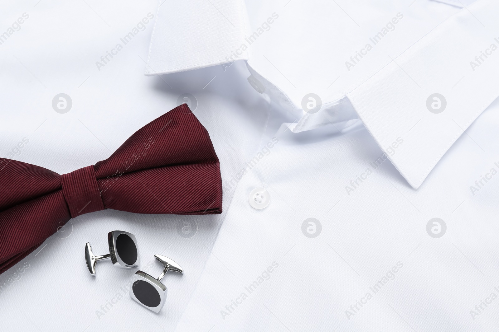 Photo of Stylish burgundy bow tie and cufflinks on white shirt, top view
