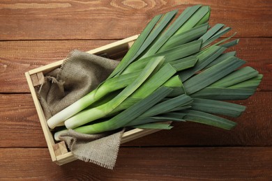 Fresh raw leeks in crate on wooden table, top view