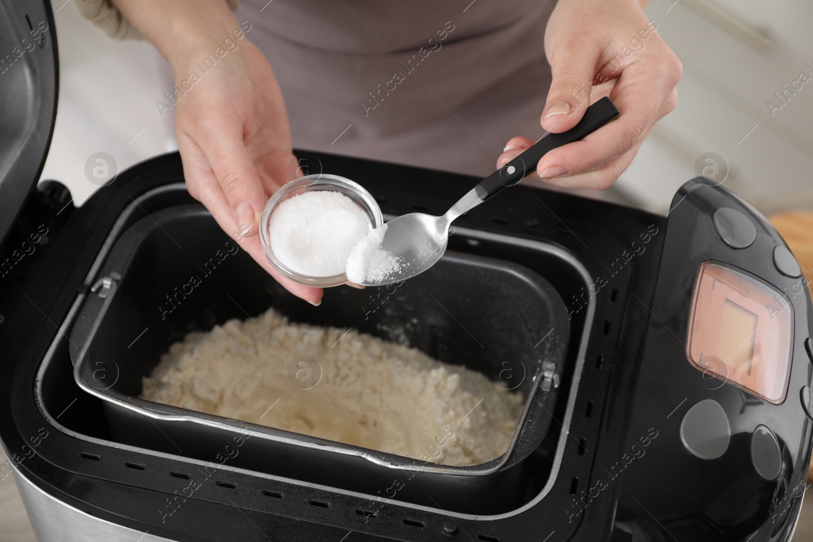 Photo of Making dough. Woman adding salt into breadmaker machine, closeup