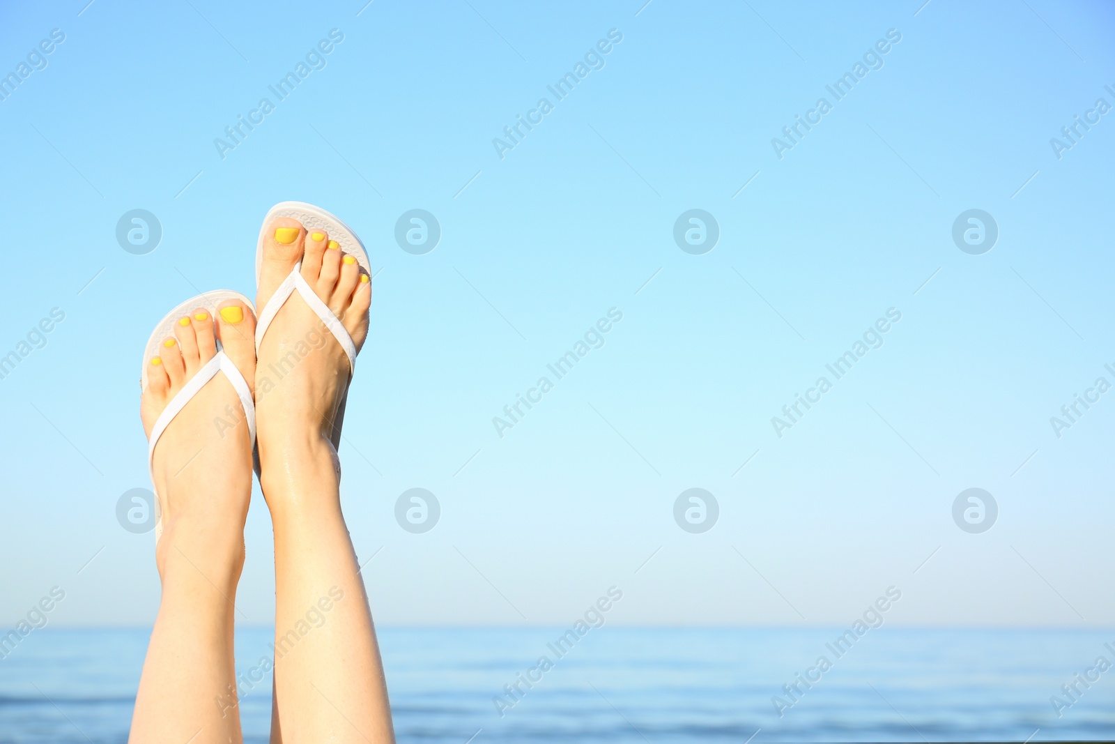 Photo of Closeup of woman wearing flip flops near sea, space for text. Beach accessories