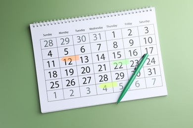 Photo of Timetable. Calendar page with marked dates and pen on green background, top view