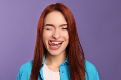 Photo of Beautiful woman with red dyed hair winking on purple background