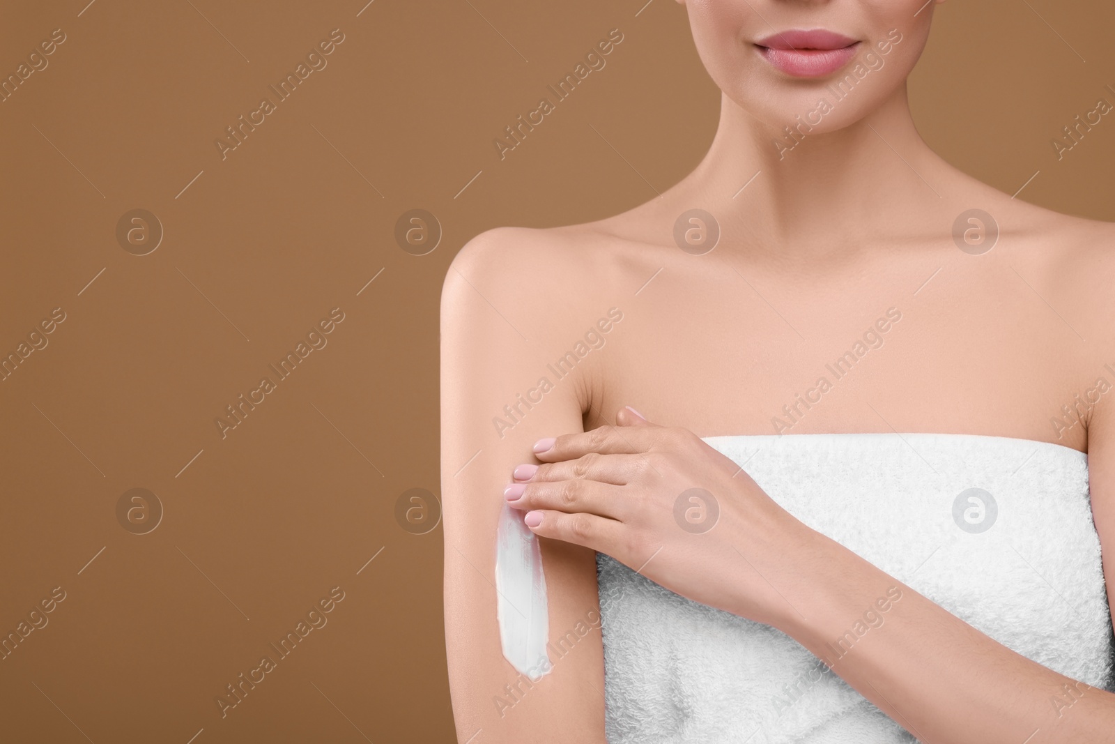 Photo of Woman with smear of body cream on her arm against light brown background, closeup. Space for text