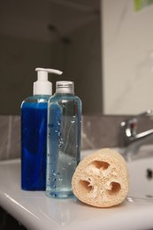 Photo of Natural loofah sponge and shower gel bottles on washbasin in bathroom