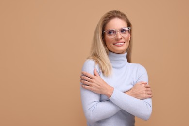 Photo of Portrait of smiling middle aged woman in glasses with crossed arms on beige background. Space for text