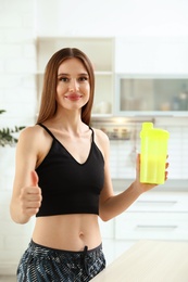 Young woman with bottle of protein shake in kitchen