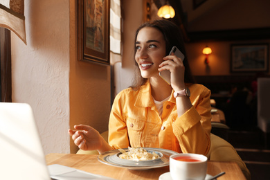 Young blogger talking on phone at table in cafe