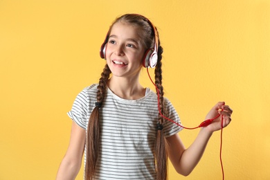 Cute little girl listening to music with headphones on color background