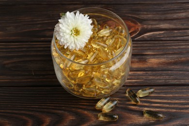 Photo of Glass medical bottle with yellow capsules and white flower on wooden table