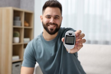 Photo of Diabetes test. Smiling man showing glucometer at home, selective focus