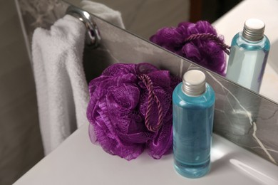 Photo of Purple shower puff and bottle of body wash gel on sink in bathroom