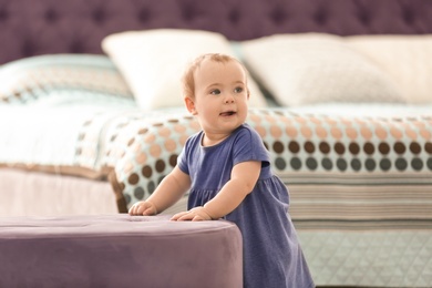 Photo of Cute baby holding on to ottoman in bedroom. Learning to walk
