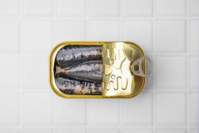 Photo of Open tin can with mackerel fillets on white tiled table, top view