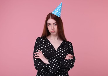 Sad woman in party hat on pink background