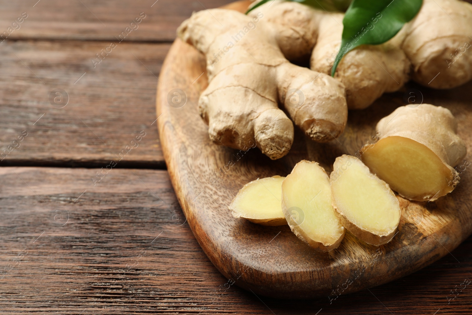 Photo of Cut and whole fresh ginger with leaves on wooden table, closeup. Space for text