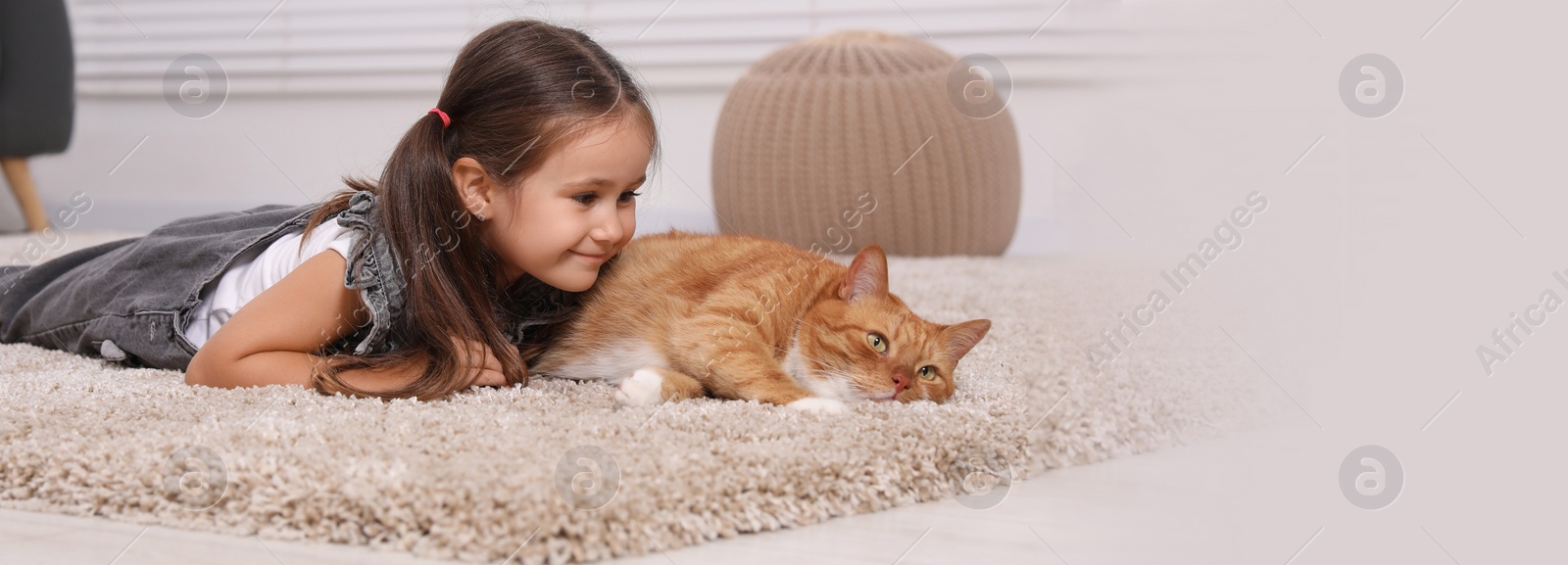 Image of Smiling little girl and cute ginger cat on carpet at home. Banner design with space for text