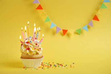 Birthday cupcake with candles on yellow background. Space for text