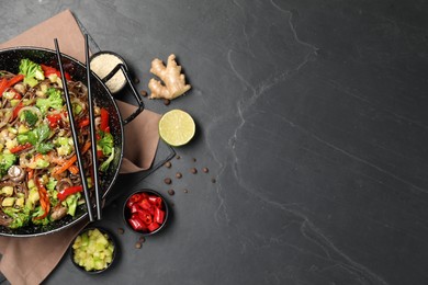 Wok with noodles, mushrooms, vegetables and other products on black table, flat lay. Space for text